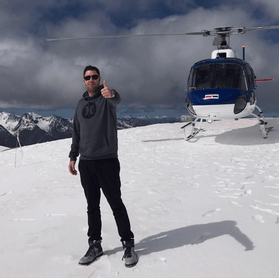 Franklin Hatchett standing on a snow covered hill with a black helicopter in the background